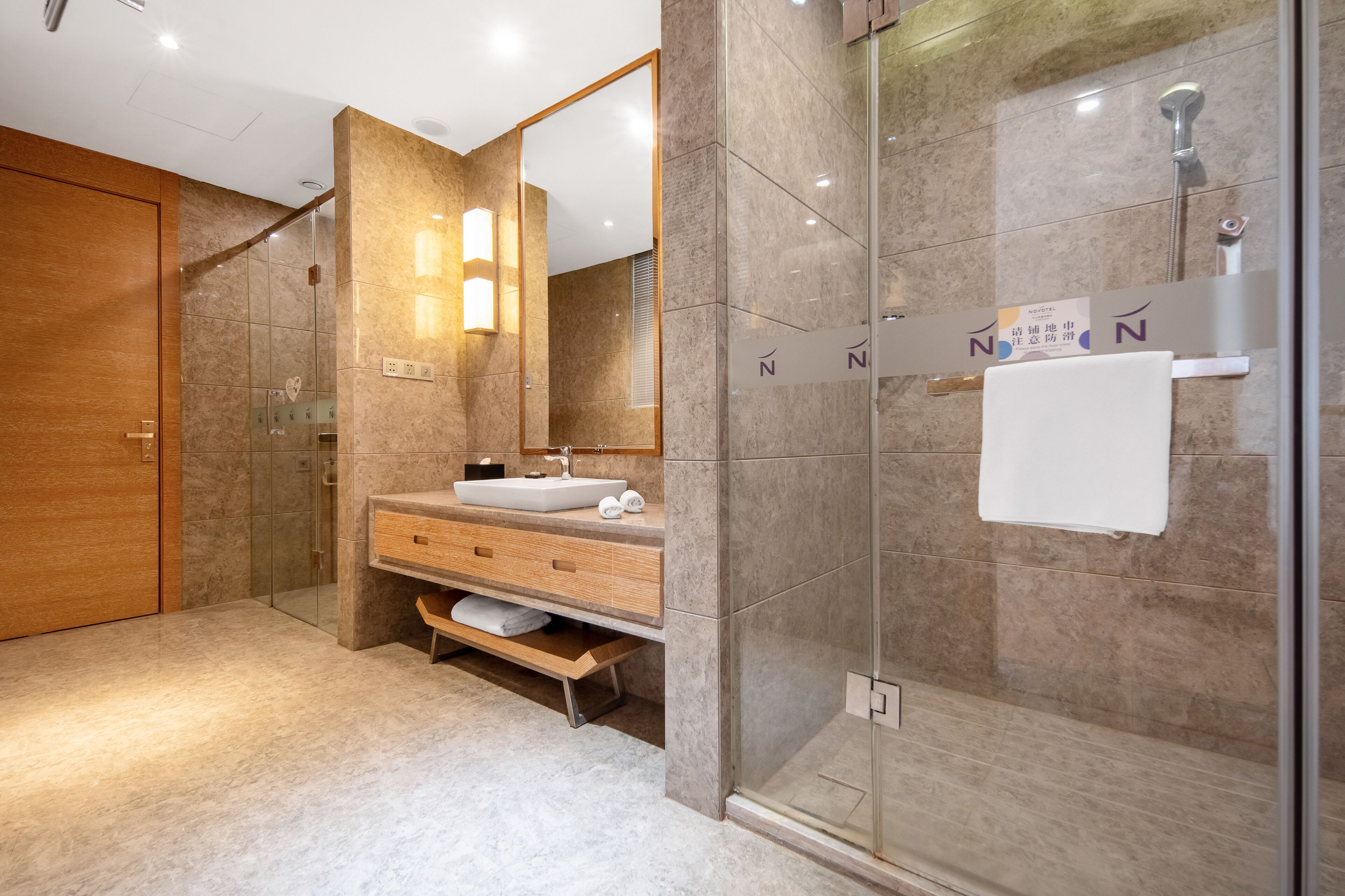 A modern bathroom with a glass shower enclosure, a wooden vanity, and a large mirror.