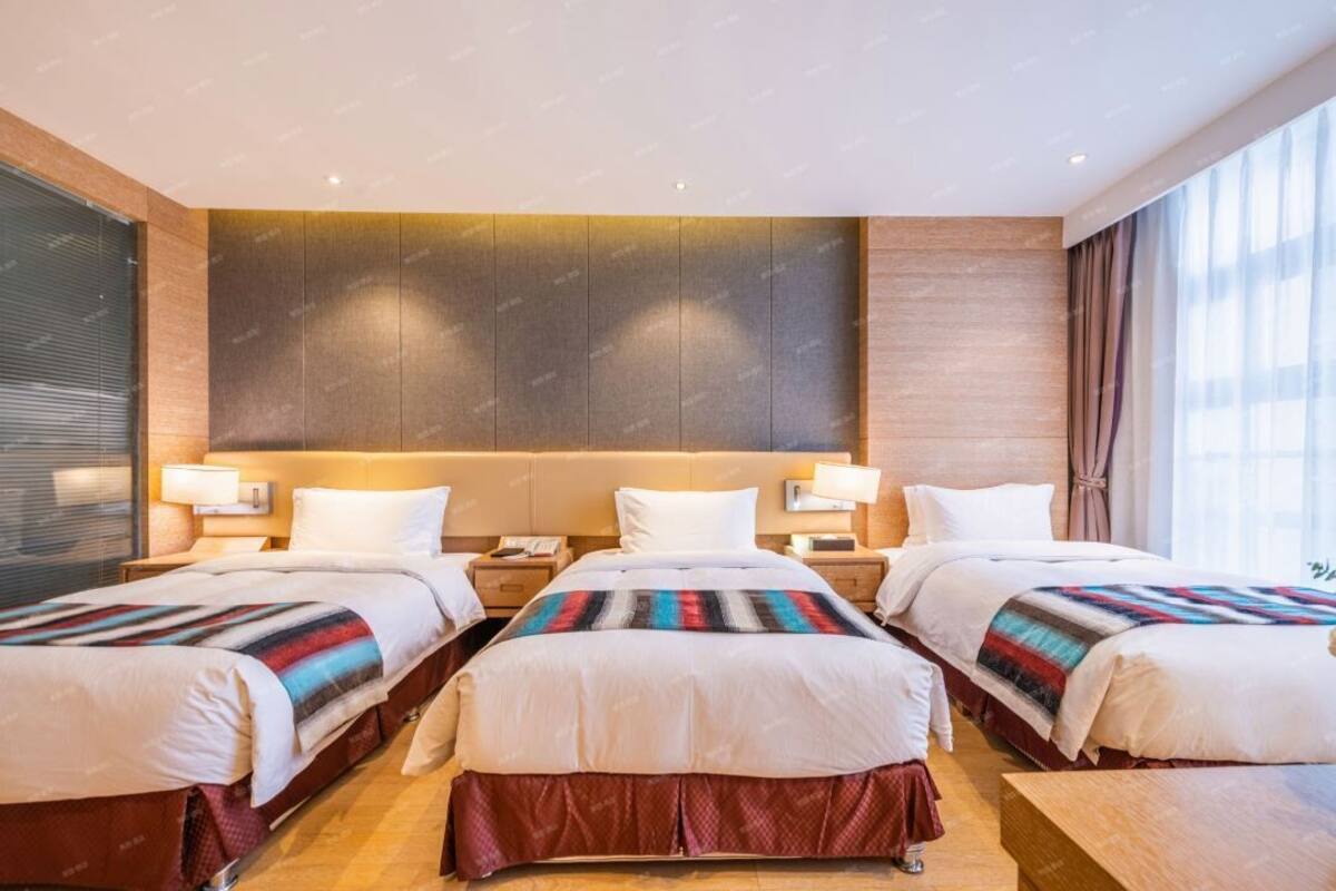 Ein Hotelzimmer mit drei Betten, jeweils mit einer gestreiften Decke, einem Holz-Kopfteil und Nachttischlampen.