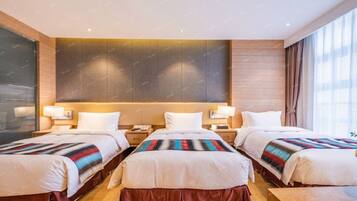 A hotel room with three beds, each with a striped blanket, wooden headboard, and bedside lamps.