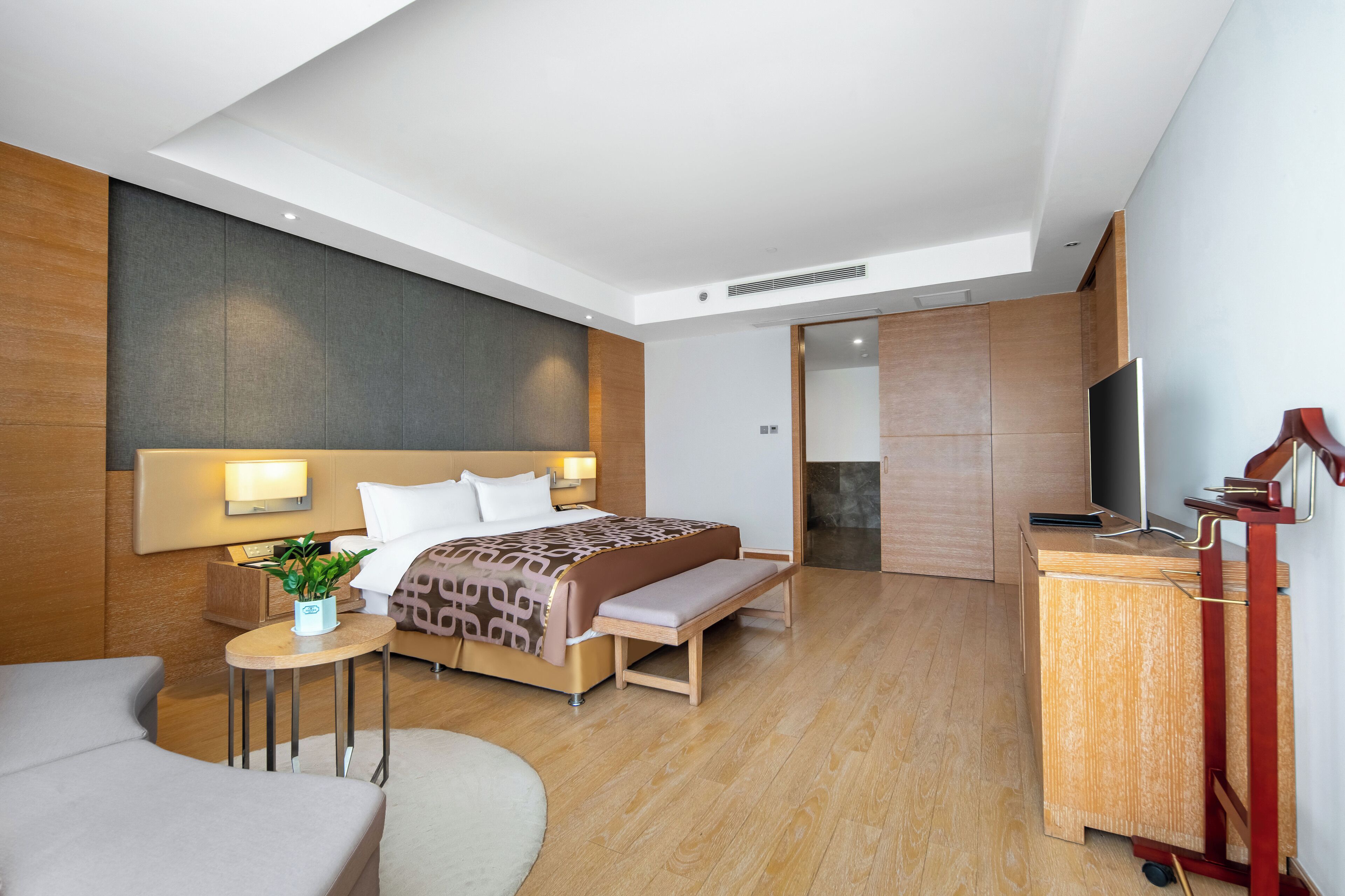 Et moderne hotelværelse med seng, sengebord, lampe, bænk og et fjernsyn på et træskab.