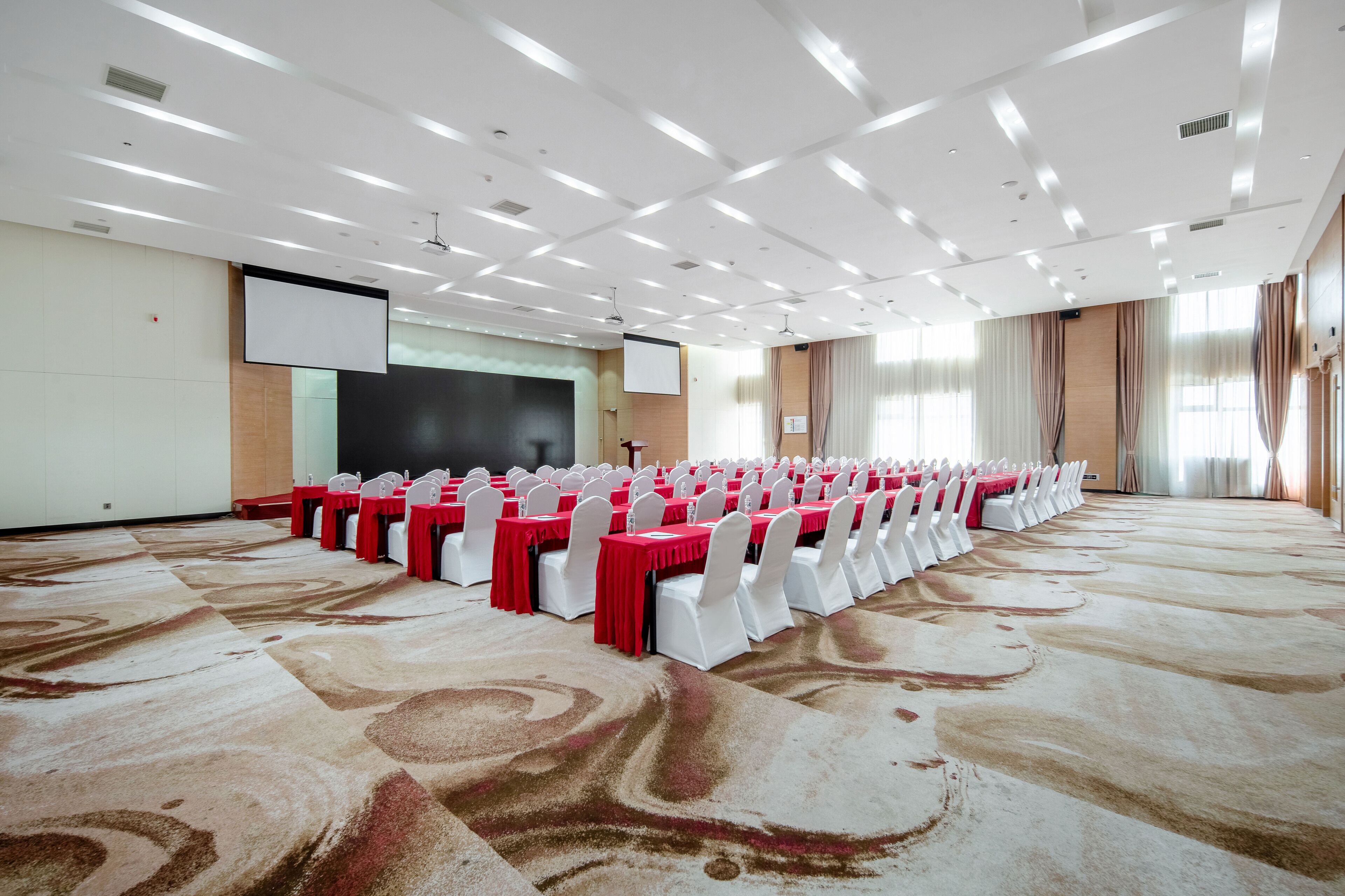 A conference room with rows of tables and chairs, a projector screen, and a carpeted floor.