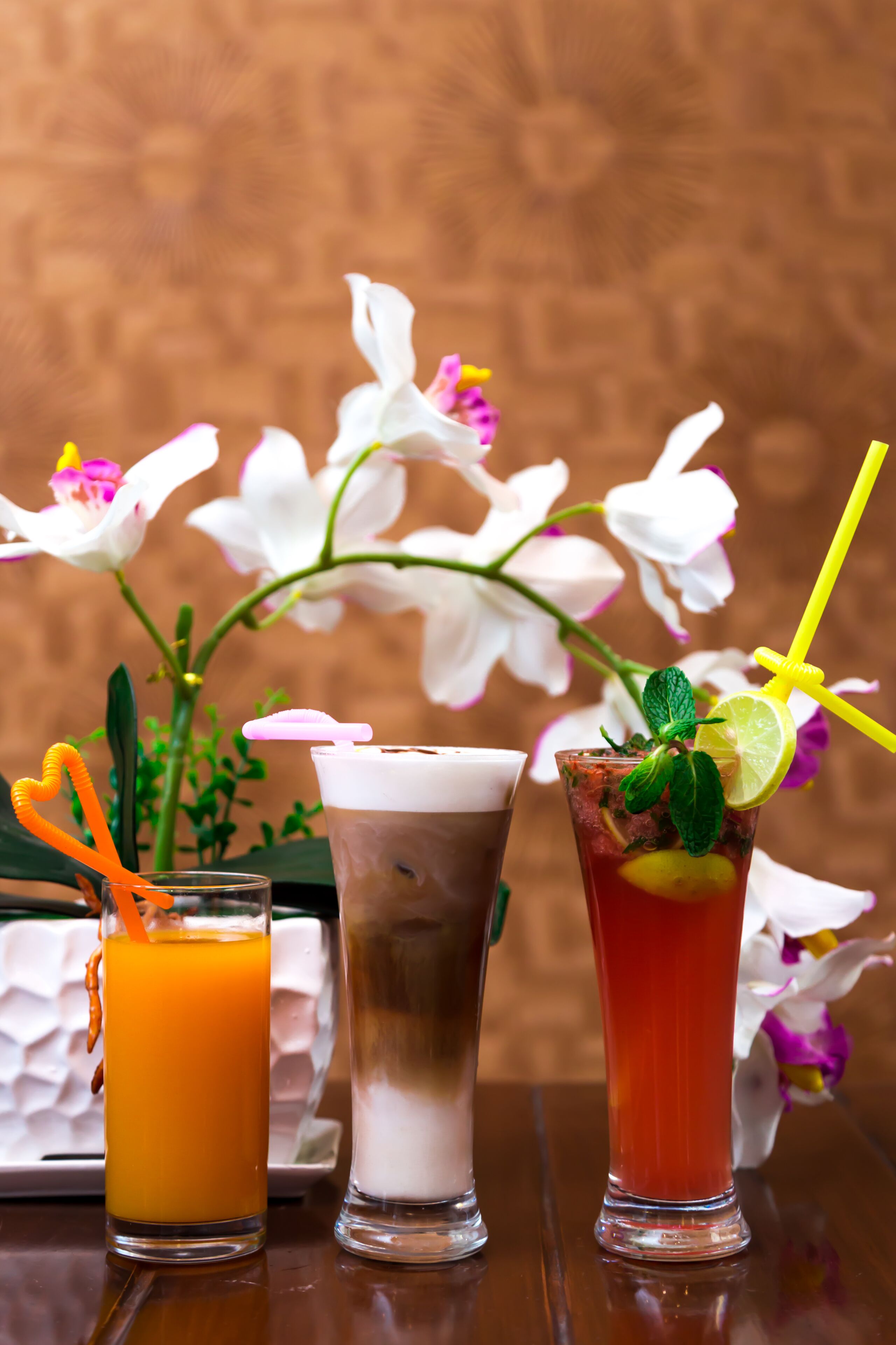 Three drinks on a table with a vase of white flowers in the background.