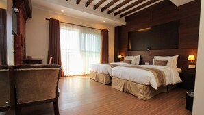 A hotel room with a large bed, a chair, wooden flooring, a TV mounted on the wall, and a window with curtains. - Sunshine Boutique Hotel (Kathmandu)