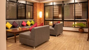 A modern lounge area with a brick accent wall, large windows, and a seating arrangement including sofas and armchairs. - Sunshine Boutique Hotel (Kathmandu)