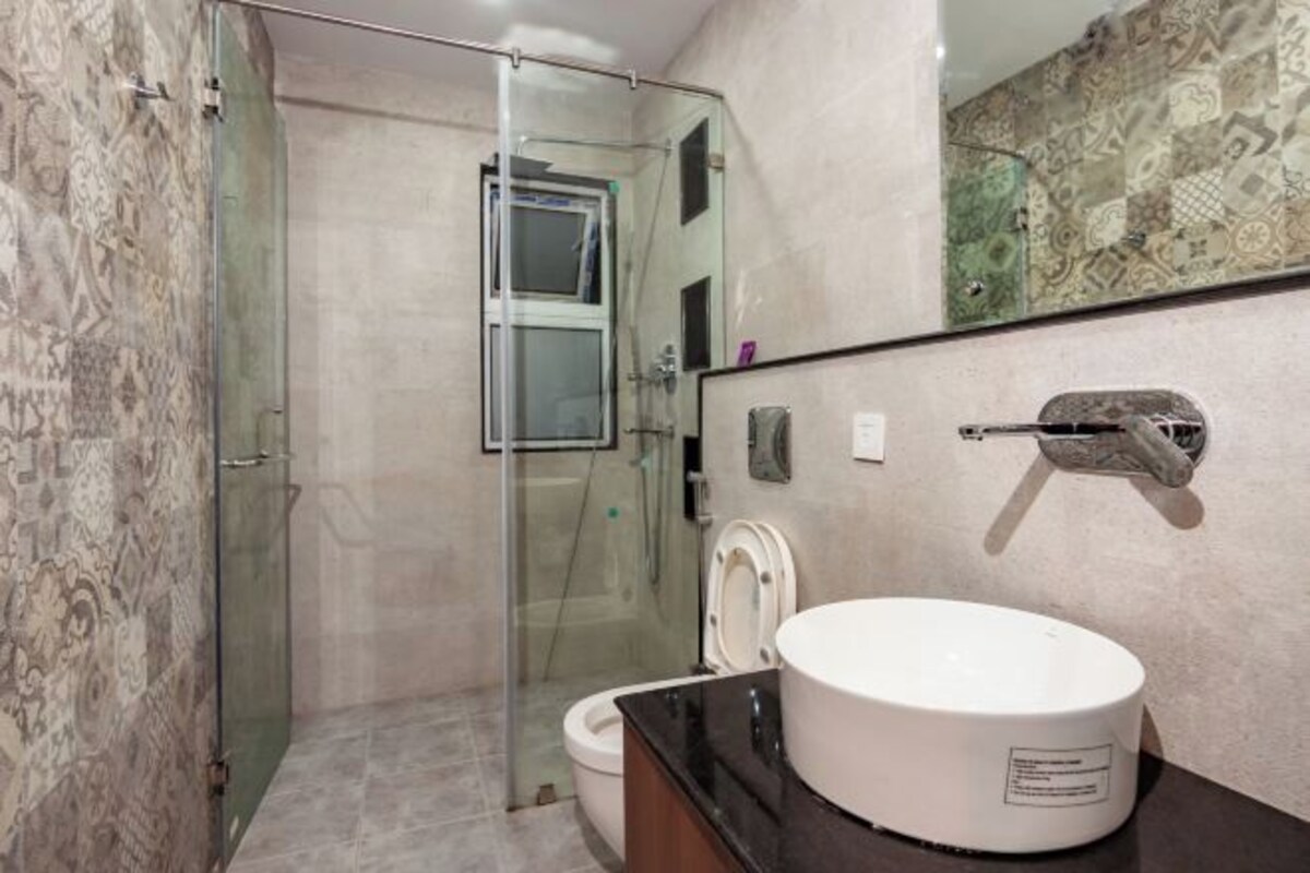 Un baño moderno con cabina de ducha de vidrio, inodoro blanco y un espejo grande con detalles de azulejos decorativos.