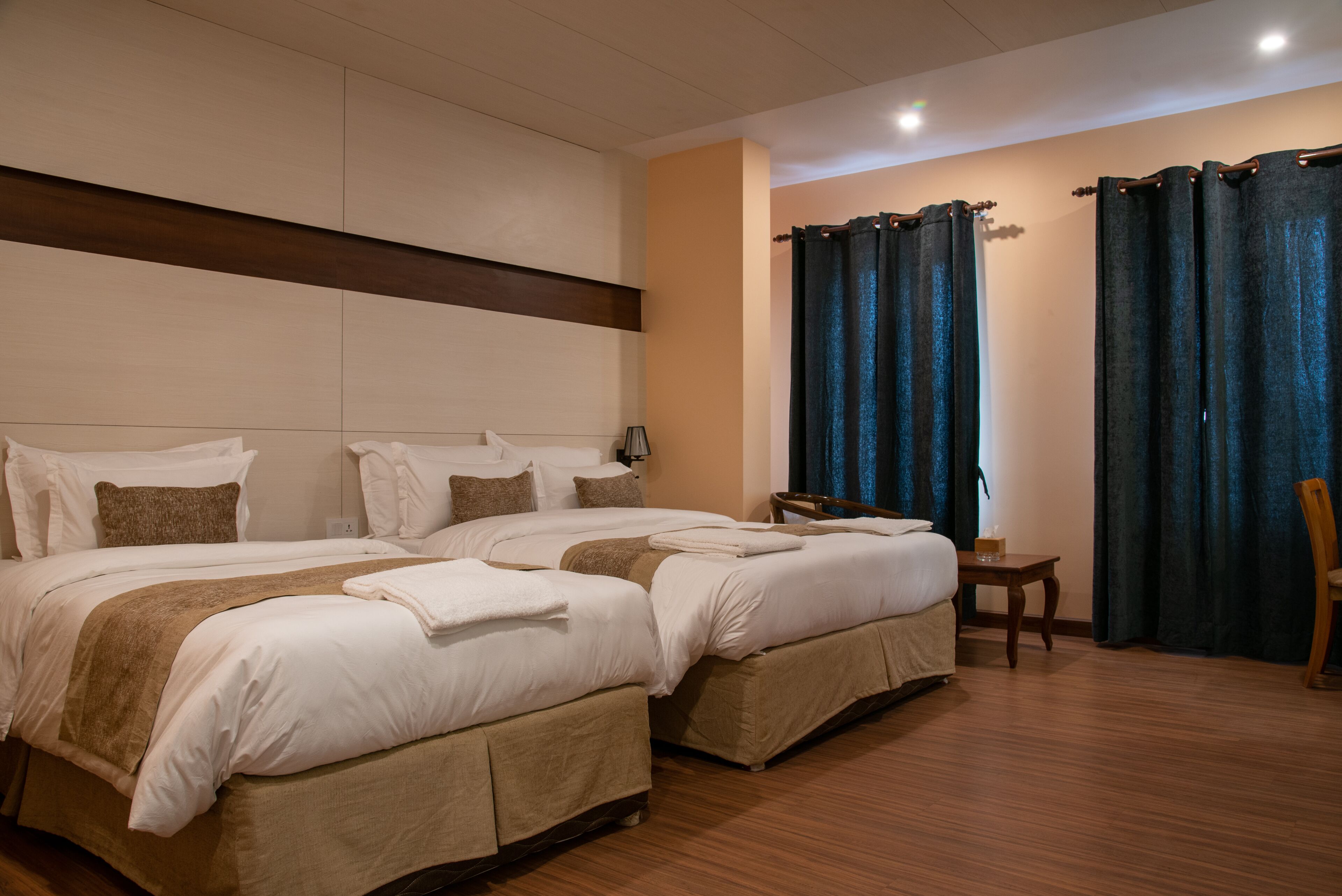 A hotel room with two beds, a wooden floor, a small table, and a chair.