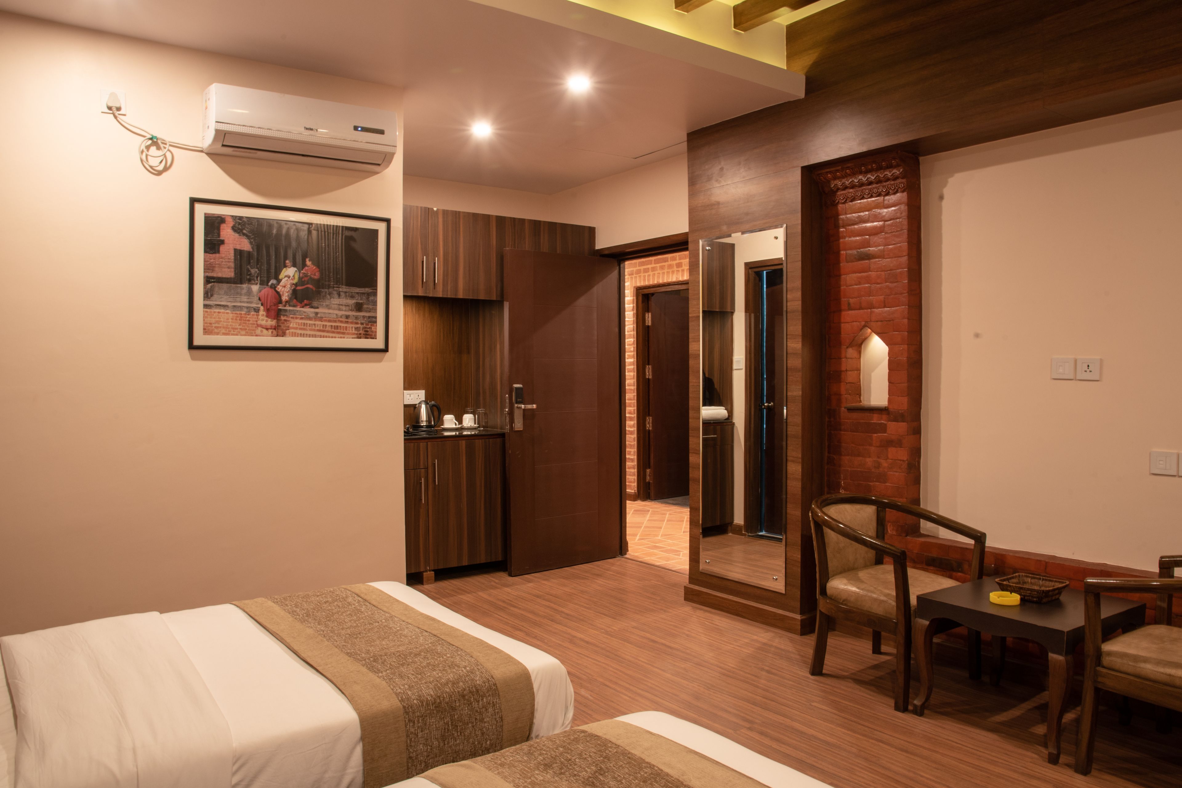 A hotel room with two beds, a small kitchenette, a mirror, and a dining area with chairs.
