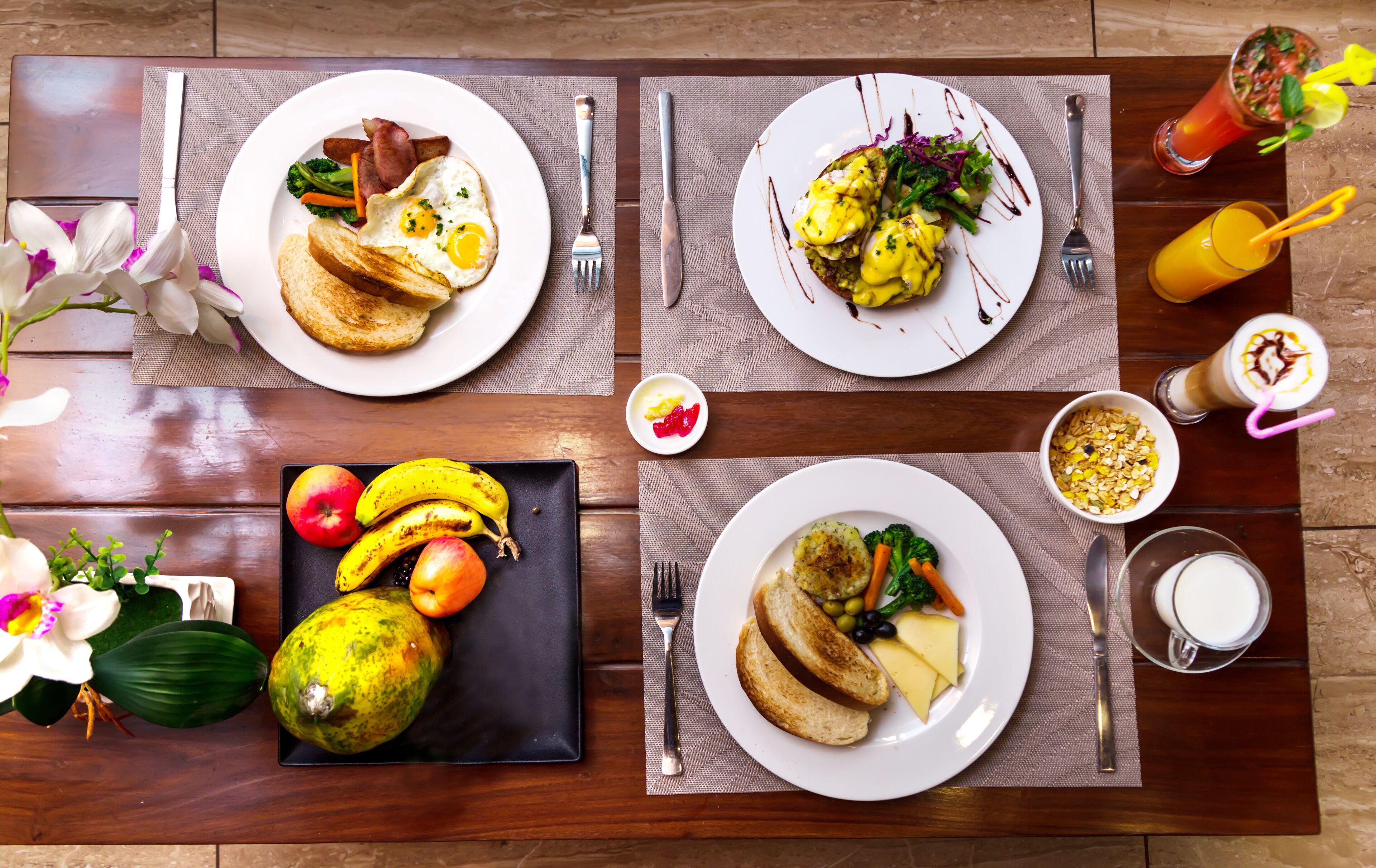 A breakfast setting with plates of food, a fruit platter, and drinks on a wooden table.