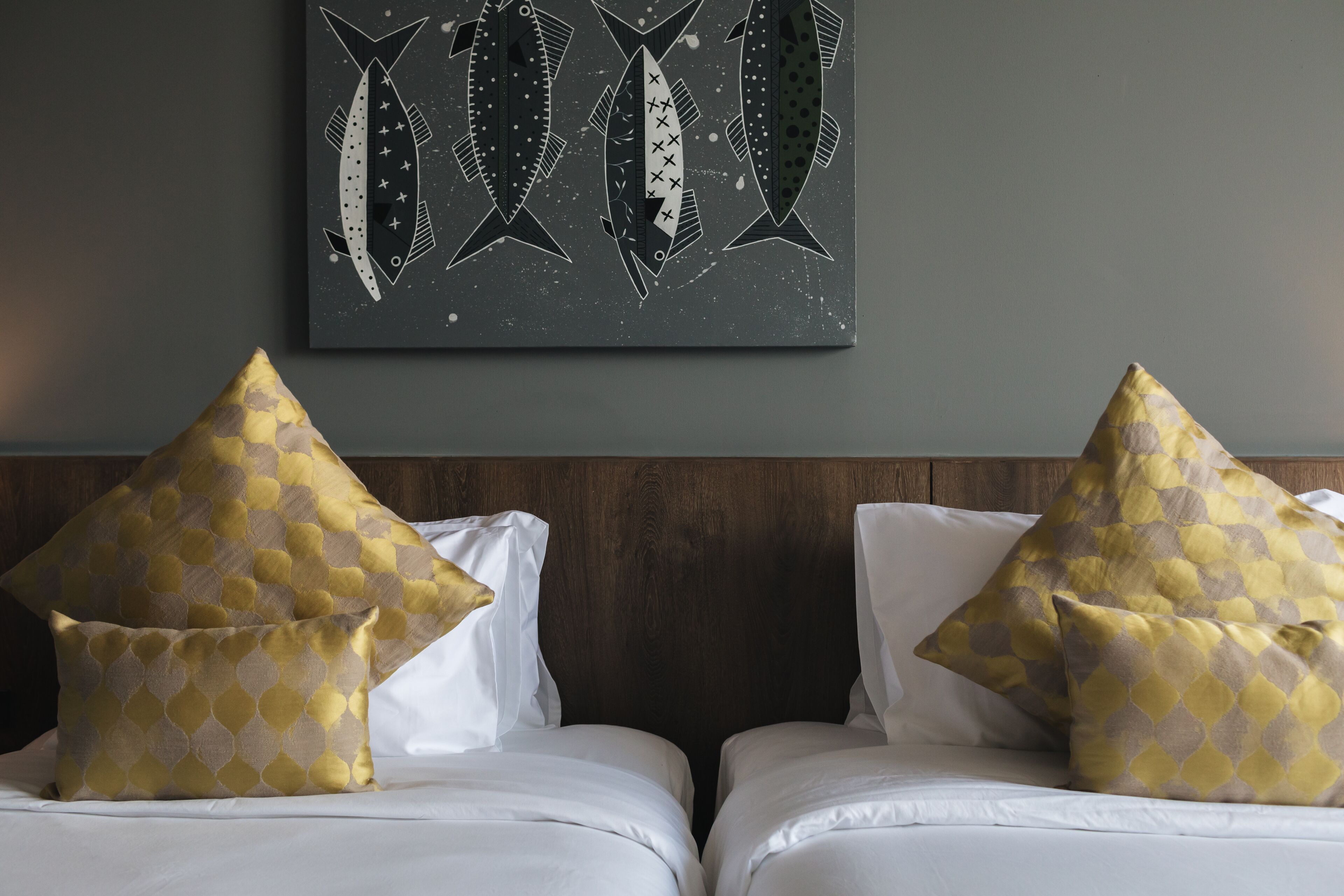 A hotel room with two beds, each with a patterned pillow and a framed artwork above.