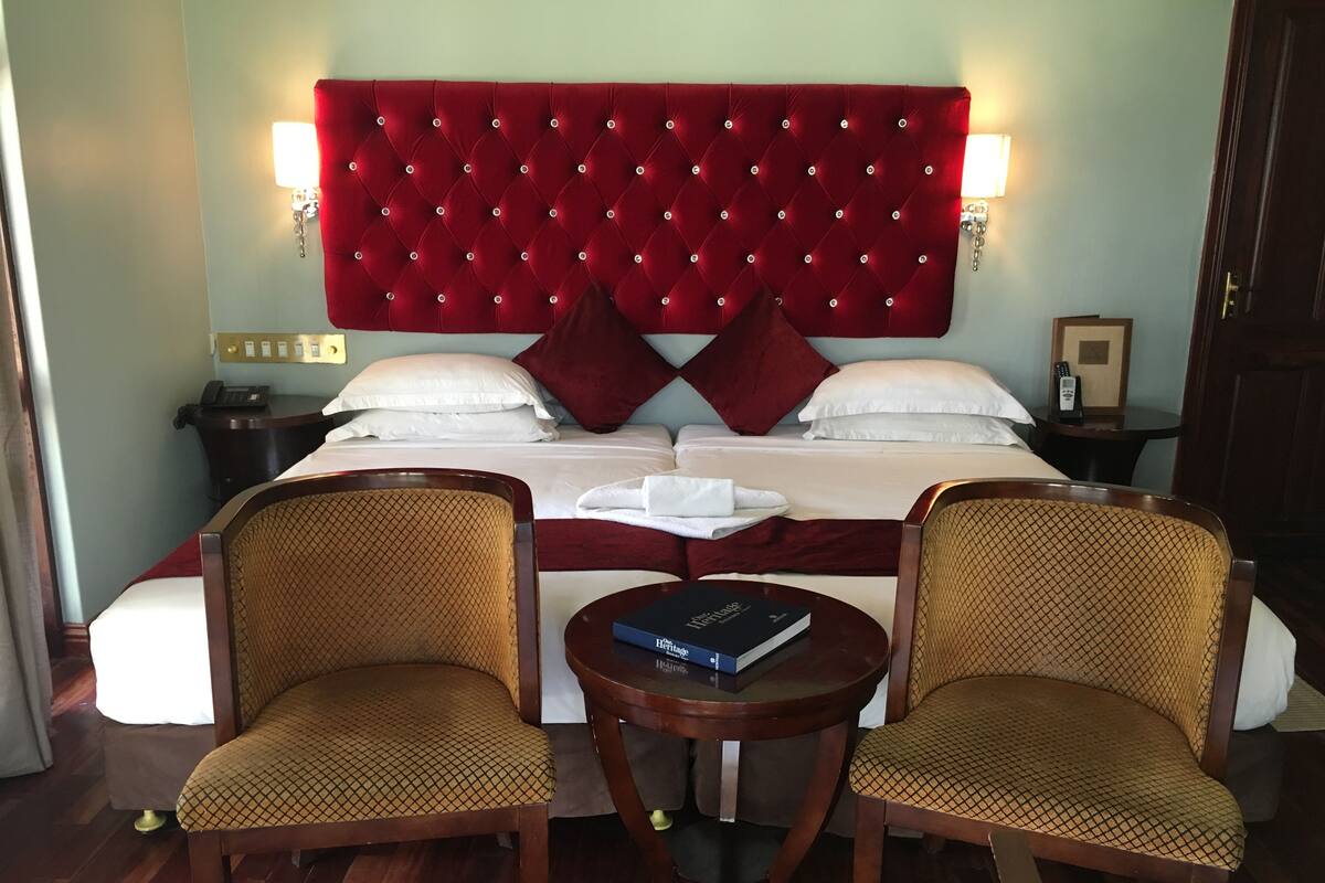 Ein Hotelzimmer mit einem großen Bett, zwei Polstersesseln, einem kleinen runden Tisch und einem roten, gepolsterten Kopfteil.