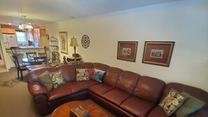 A living room with a brown leather sectional sofa, a wooden coffee table, and a kitchen in the background. - Little Black Bear Condo (Helen)