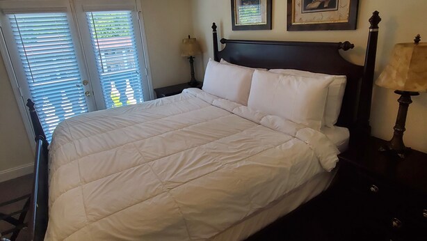A neatly made bed with a headboard, a nightstand with a lamp, and two framed pictures on the wall. - Little Black Bear Condo (Helen)