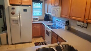 A compact kitchen with wooden cabinets, a refrigerator, a toaster, and a coffee maker. - Little Black Bear Condo (Helen)