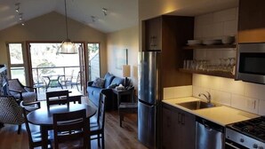 A modern kitchen with stainless steel appliances, a dining area with wooden furniture, and a view to the outside. - Two Bedroom Oceanfront Villa - Mayne Island Resort (Mayne Island)