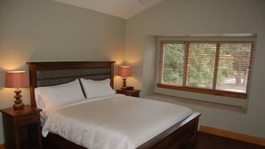 A bedroom with a large bed, two bedside tables with lamps, and a window with blinds. - Two Bedroom Oceanfront Villa - Mayne Island Resort (Mayne Island)
