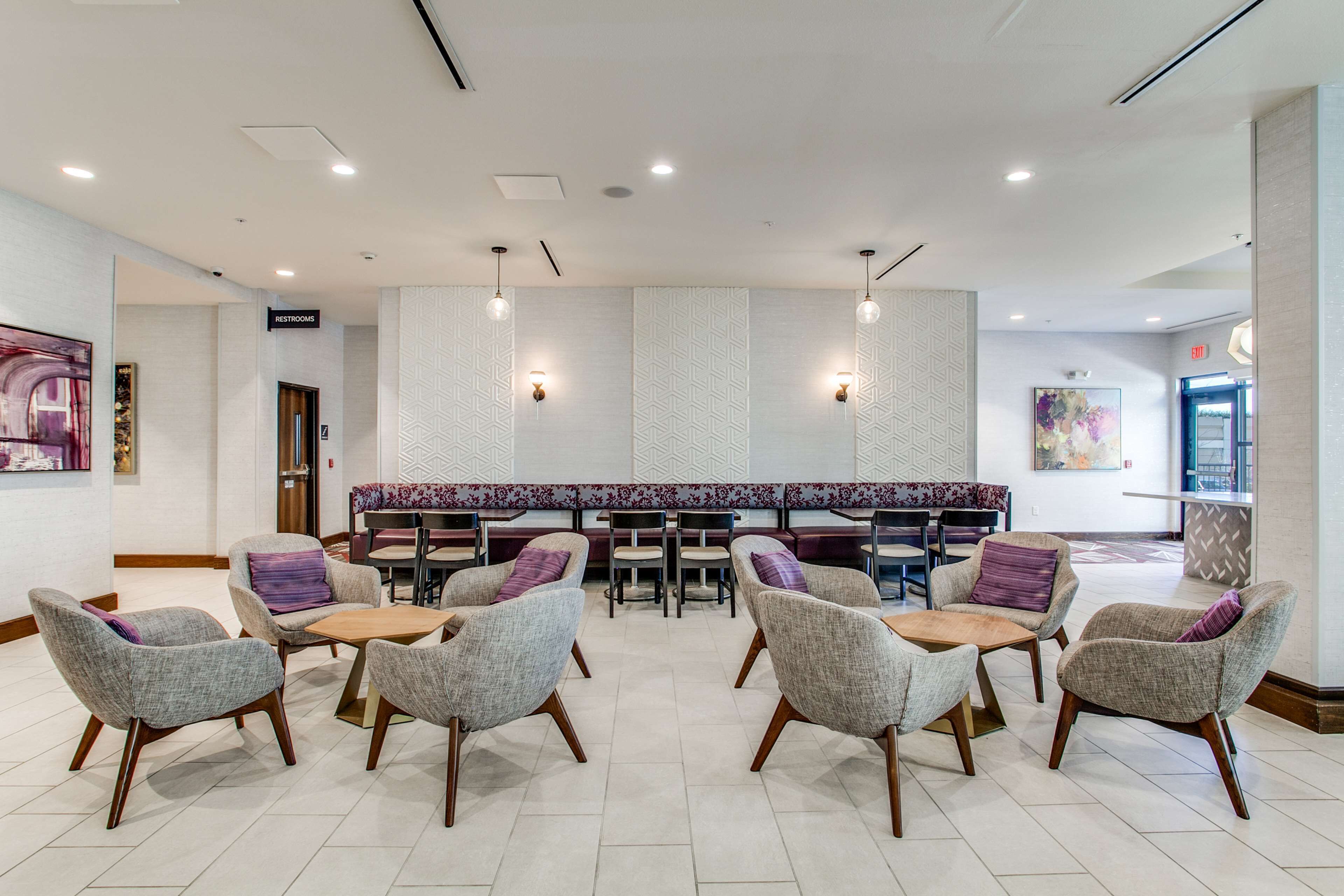 A modern lobby with a seating area, a reception desk, and a sign indicating restrooms.