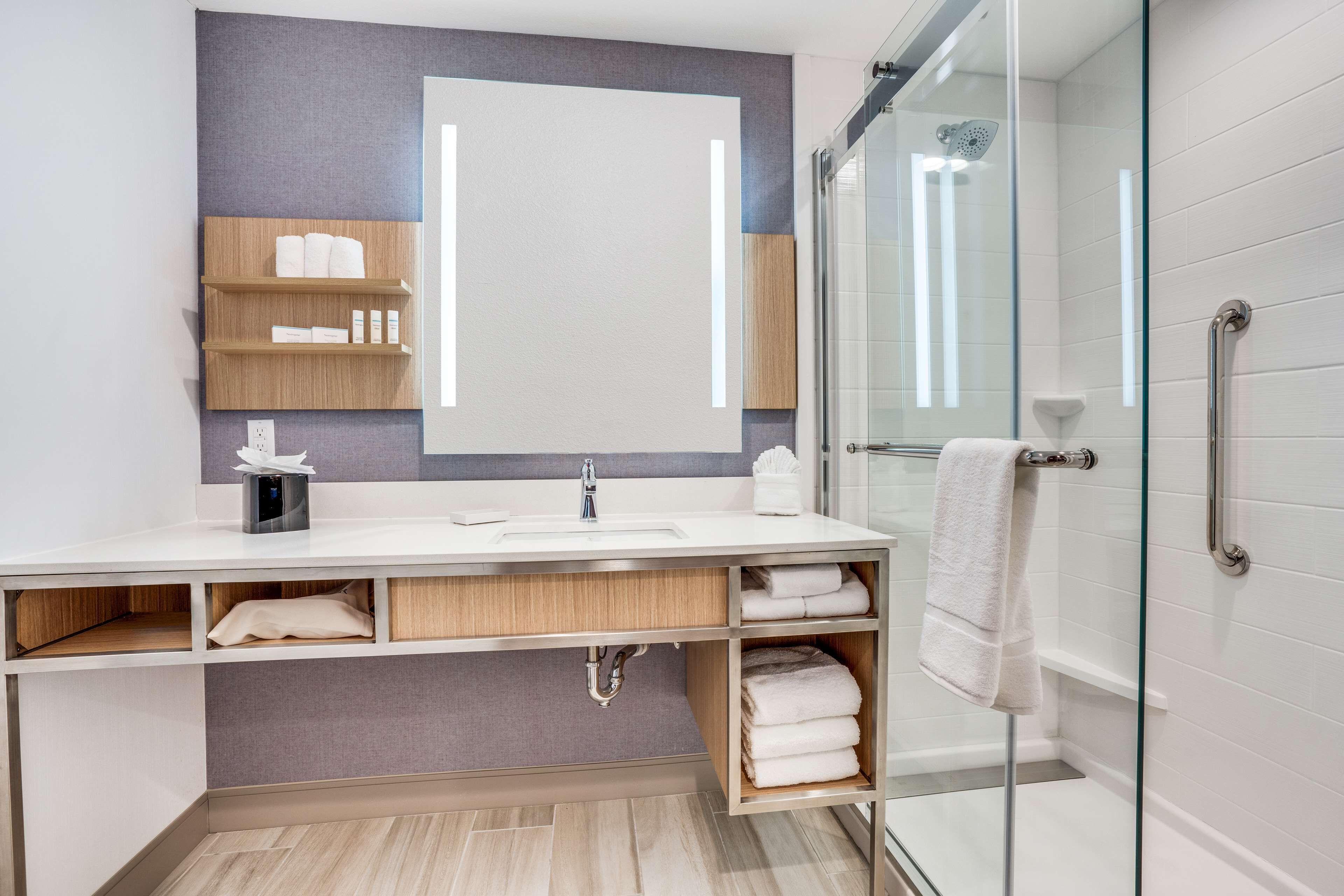A modern bathroom with a large mirror, white sink, and glass shower enclosure.
