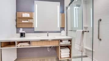 A modern bathroom with a large mirror, white sink, and glass shower enclosure.