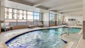 A modern indoor pool area with clear views through large windows, a jacuzzi, and seating by the pool. - Hilton Garden Inn North Dallas Central Expy (Dallas)