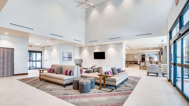 A spacious lobby with a high ceiling, modern furniture, and a large window providing natural light. - Hilton Garden Inn North Dallas Central Expy (Dallas)
