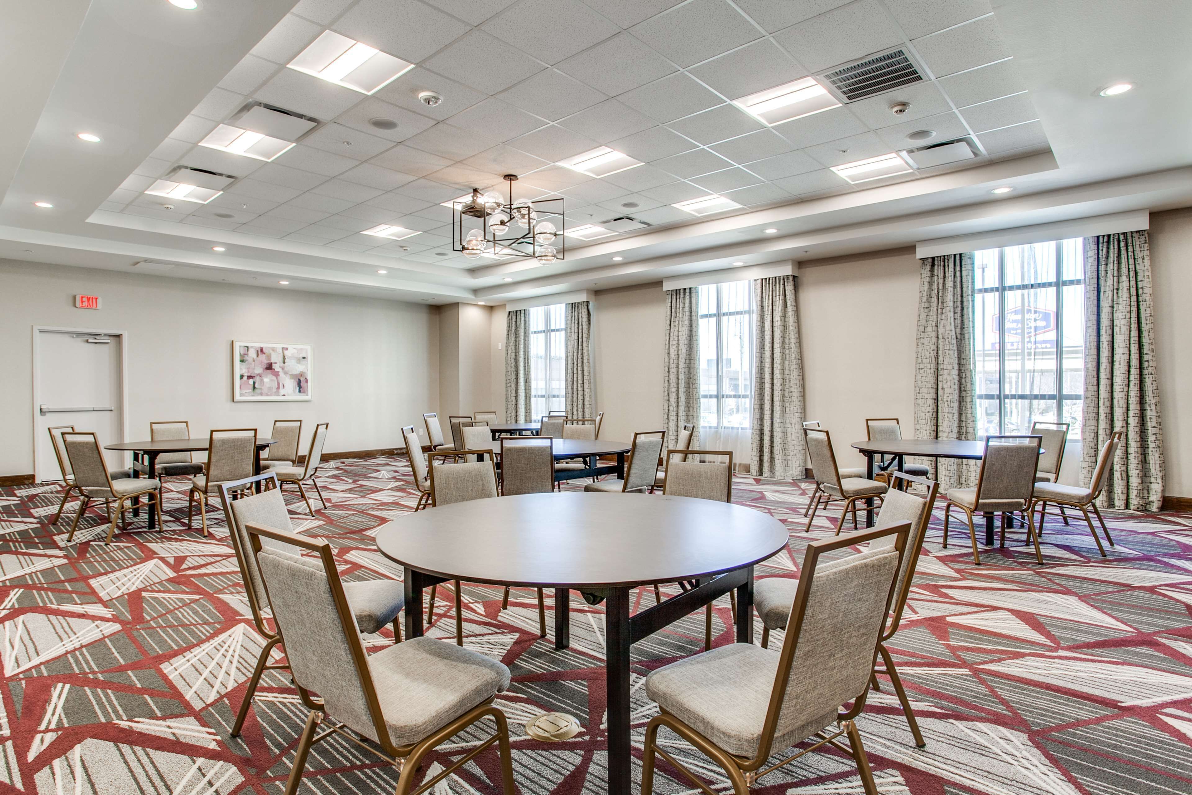 Une salle de conférence dotée d’une grande table ronde entourée de chaises, de grandes fenêtres avec des rideaux et d’un tapis à motifs.