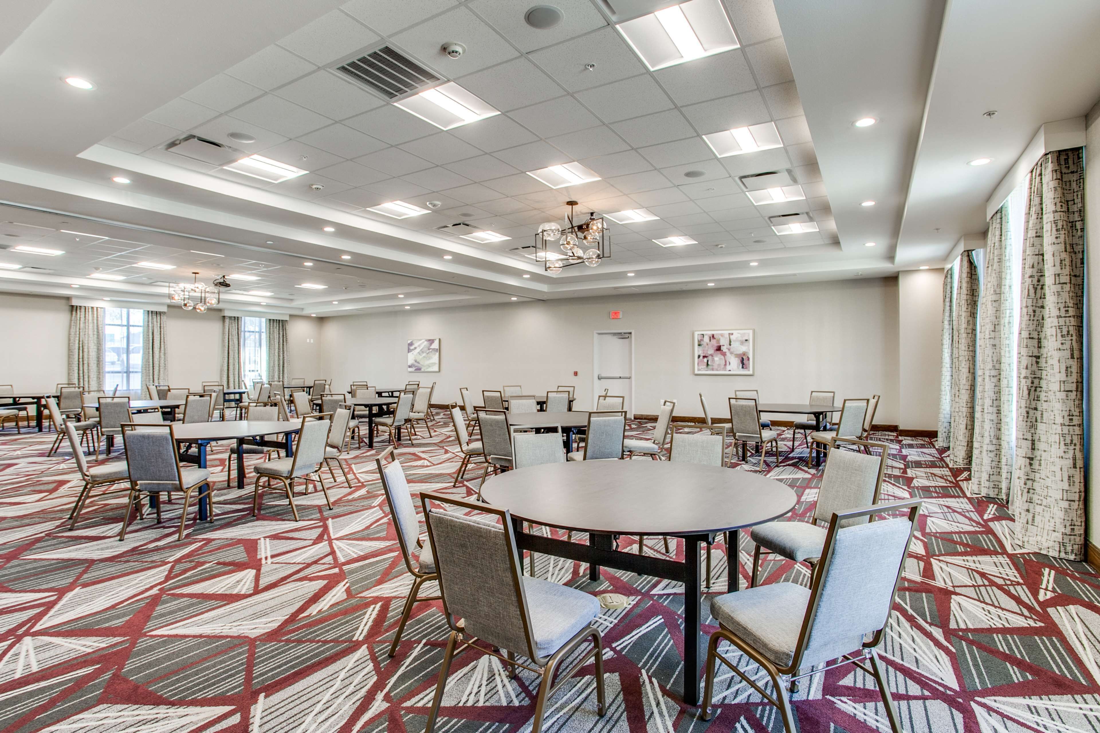 A large conference room with multiple tables and chairs, a patterned carpet, and a ceiling with recessed lighting.