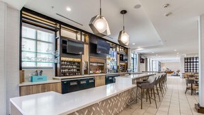 A modern bar area with a long counter, bar stools, and a variety of beverages and glassware. - Hilton Garden Inn North Dallas Central Expy (Dallas)