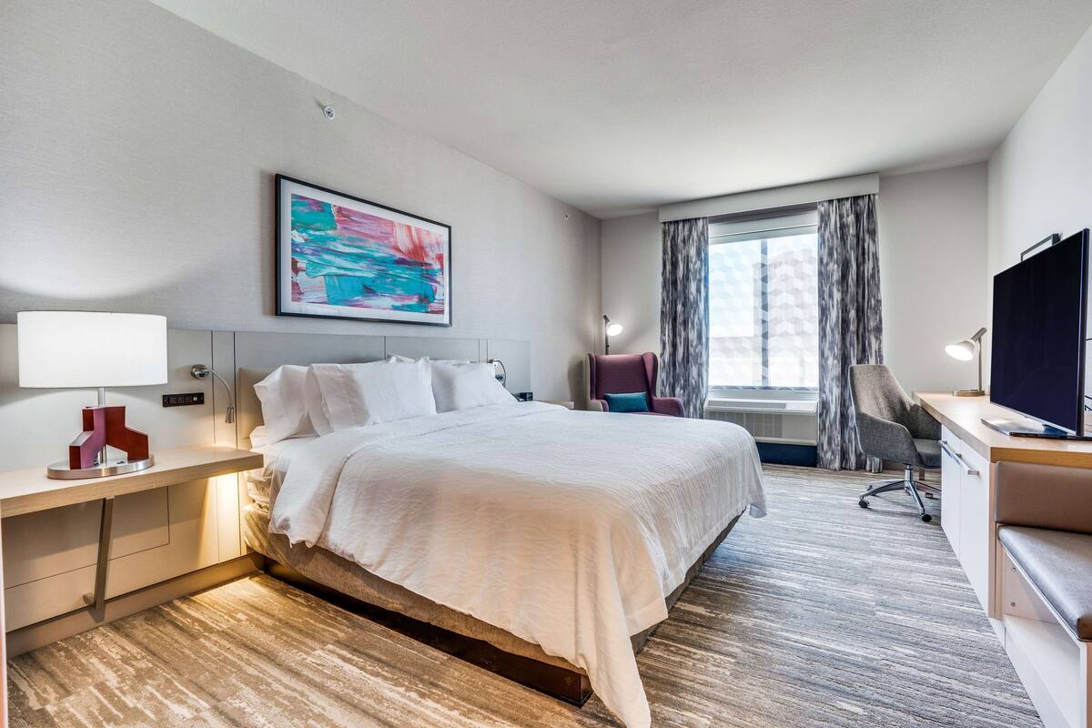 Een hotelkamer met een bed, bureau, stoel, televisie en kunst aan de muur.