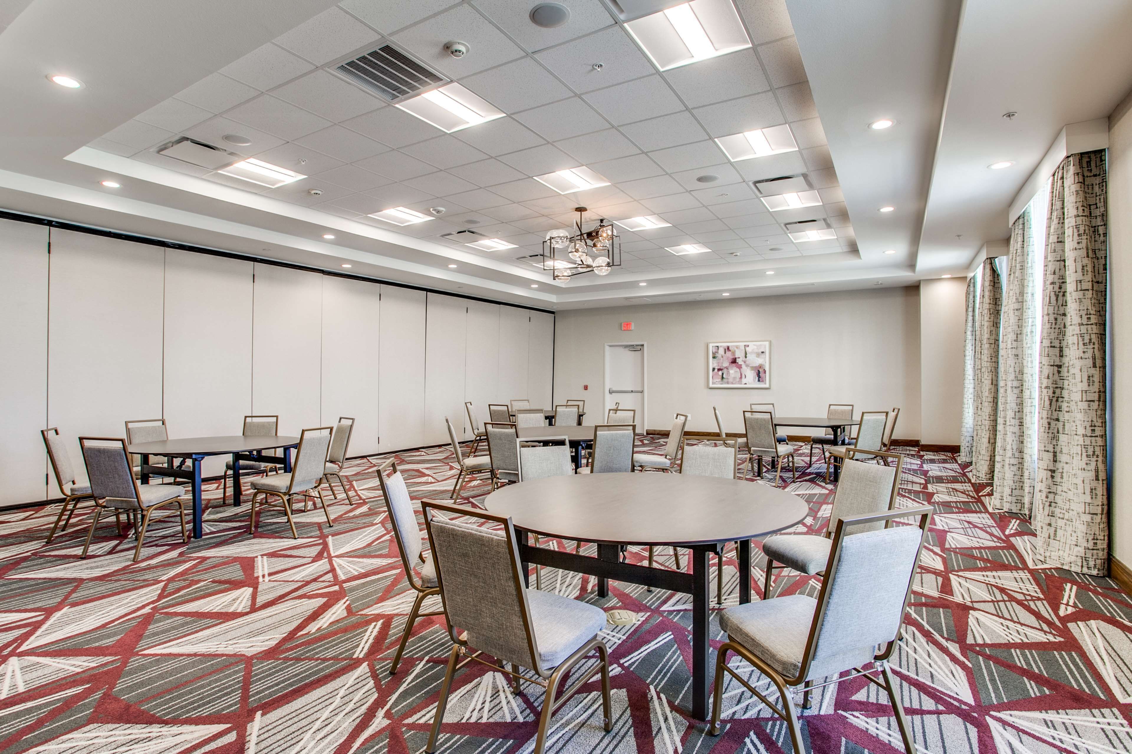 A conference room with a round table, multiple chairs, a patterned carpet, and a ceiling with recessed lighting.