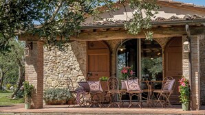 Un edificio de piedra con un patio cubierto, mesas al aire libre y plantas en macetas.