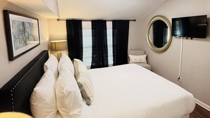 A hotel room with a large bed, a bedside table with a lamp, a TV mounted on the wall, and a window with curtains. - Posh spacious pool house in the Heights. (Tampa)