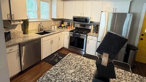 A modern kitchen with white cabinets, stainless steel appliances, a granite countertop, and a black chair. - Posh spacious pool house in the Heights. (Tampa)