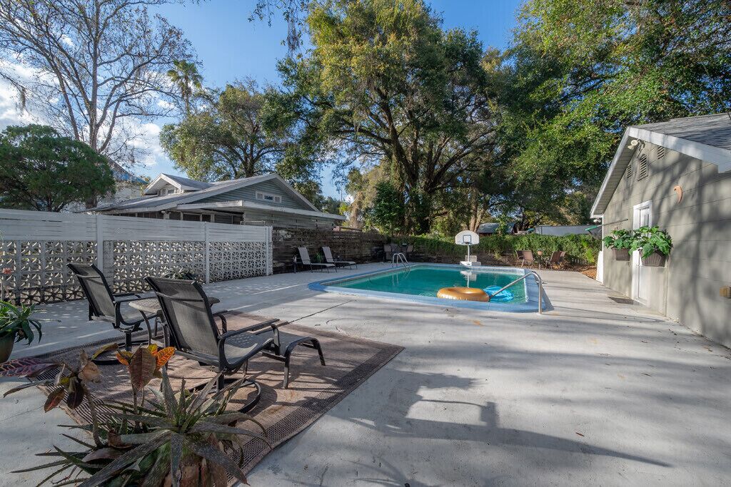 Un patio trasero con piscina, sillas de descanso y un porche cubierto.