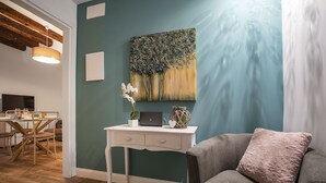 A room with a dining area, a desk with a laptop, a vase with flowers, and a grey armchair with a cushion. - Dorsoduro Suite 1241 by Wonderful Italy (Venice)
