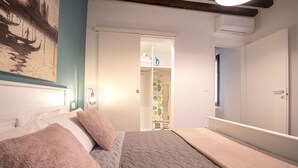 A bedroom with a bed, a nightstand, a wall-mounted air conditioner, and a door leading to a closet. - Dorsoduro Suite 1241 by Wonderful Italy (Venice)