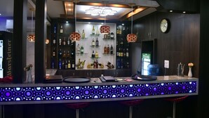A bar area with a modern design, featuring a patterned countertop, hanging pendant lights, and shelves stocked with various bottles. - Marinha Airport Hotel (Kathmandu)