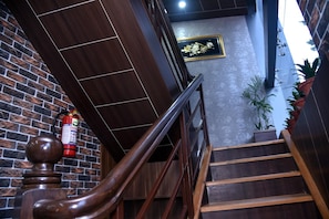 A wooden staircase with a handrail, a fire extinguisher, and a brick wall. - Marinha Airport Hotel (Kathmandu)