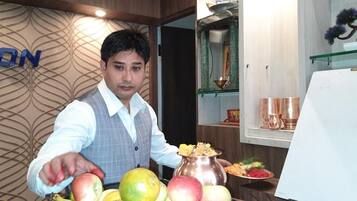 A person in a vest and shirt presenting fruits and a metal pot with food.