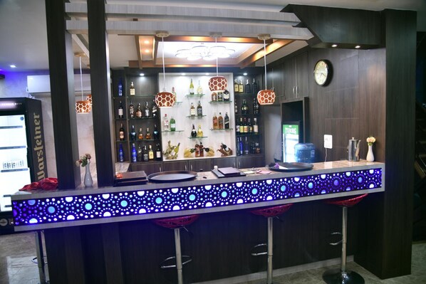 Zona de bar con mostrador, taburetes y estantes llenos de botellas.