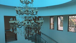 A grand chandelier hanging from the ceiling in a spacious room with a staircase and large windows. - Salerato Boutique Hotel (Gaborone)
