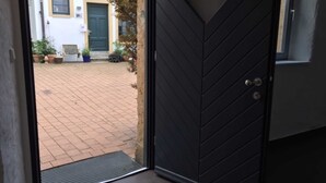 Een moderne deur met een geometrisch patroon, leidend naar een geplaveid binnenterrein met potplanten en een gebouw op de achtergrond.