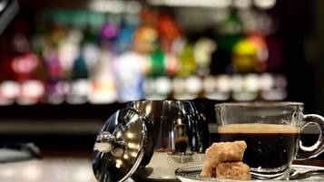 A bar setting with a coffee cup, a glass of dark liquid, and a sugar packet on a clear glass plate.