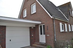 A two-story brick house with a white garage door, a front door with a small porch, and a wooden fence in the front yard.