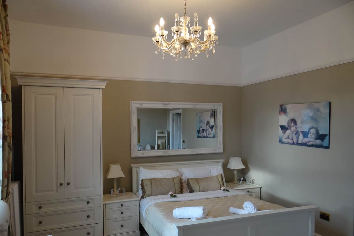 A bedroom with a large bed, a wardrobe, a mirror, and a chandelier.