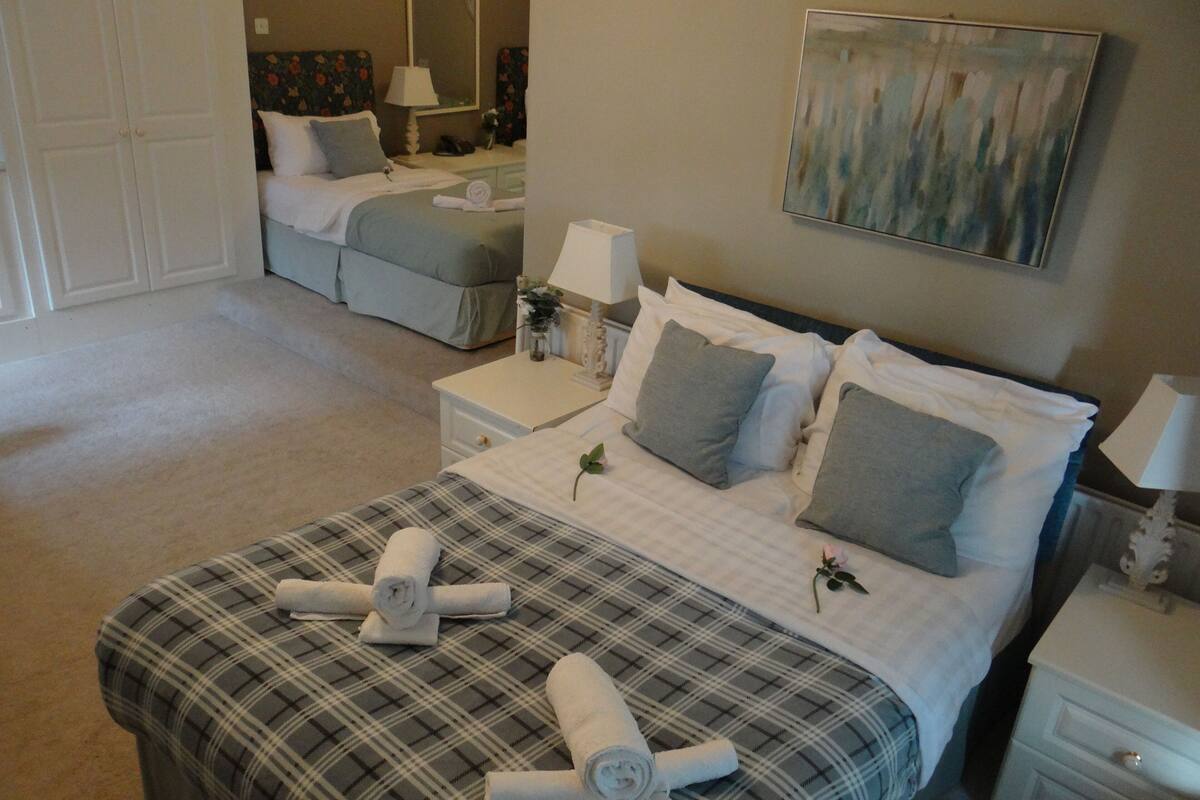 A hotel room with a large bed, a bedside table, a nightstand, a wardrobe, and a painting on the wall.