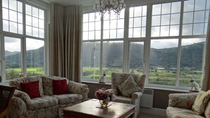 A room with large windows, floral-patterned sofas, a wooden coffee table, and a chandelier. - Plas Maenan Country House (Llanrwst)