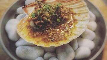 A dish of food served on a shell with a garnish, surrounded by small stones.