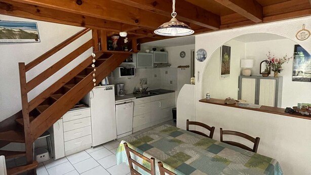 Uma cozinha acolhedora com vigas de madeira, uma mesa de jantar com cadeiras e uma escada que leva a outro andar.