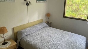 Quarto com cama, mesa de cabeceira, abajur, aquecedor fixado na parede e duas quadros emoldurados.