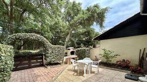 Um pátio com piso de tijolos, uma mesa com cadeiras e um forno a pizza.